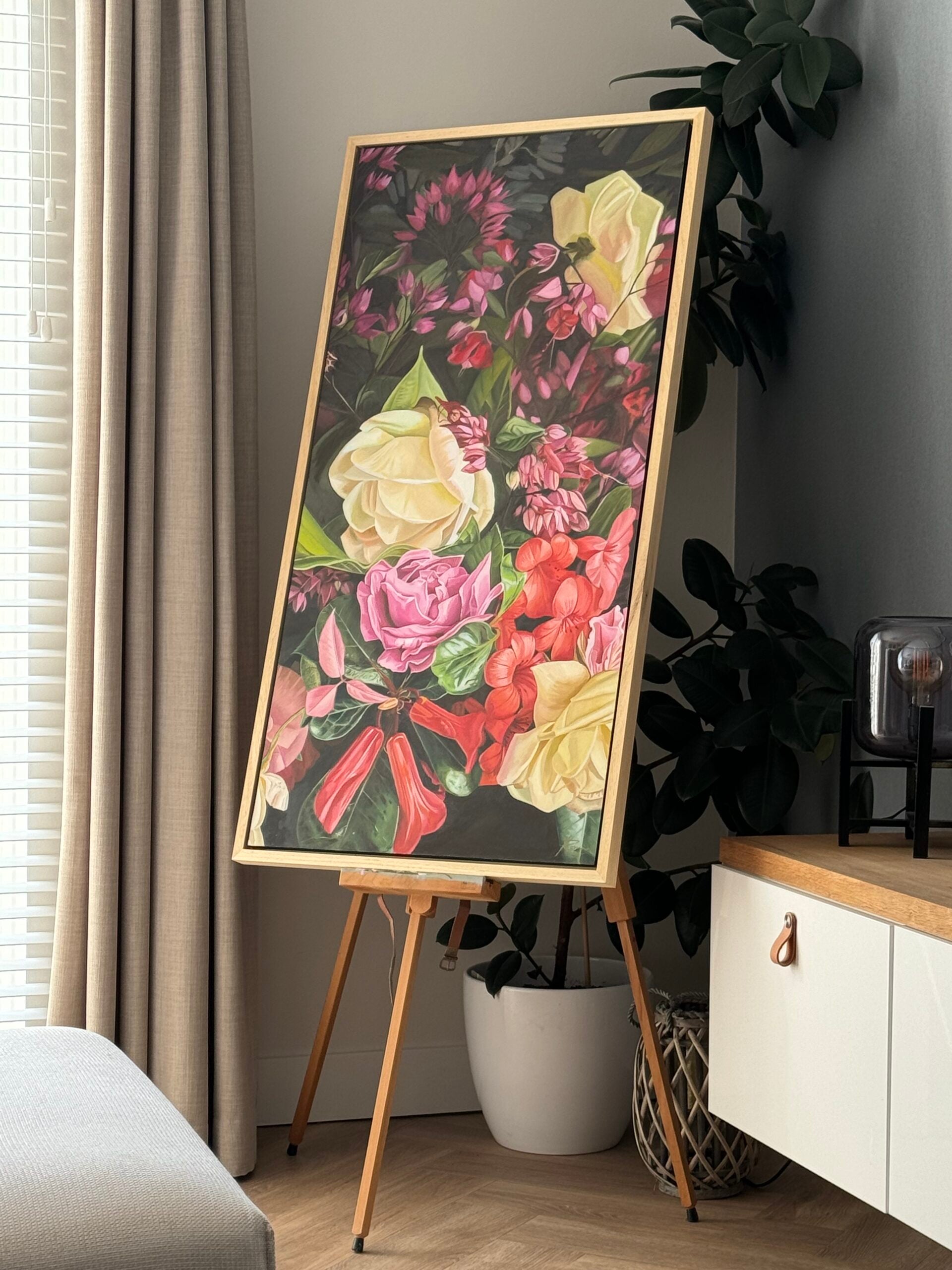 Floral painting on an easel in a room with a plant and cabinet.