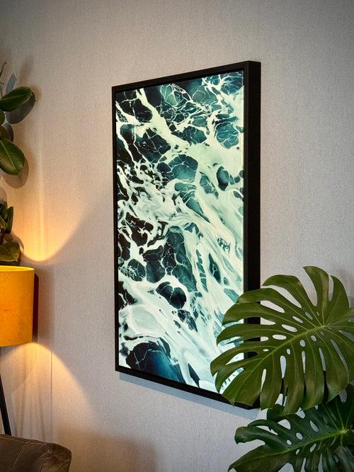 Framed abstract artwork with blue and white patterns on a canvas, surrounded by plants.