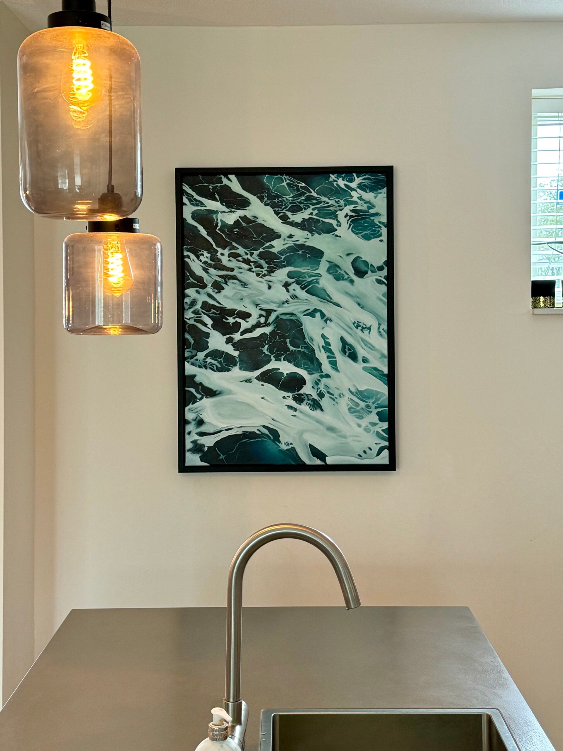 Modern kitchen with a sink, abstract art on the wall, and pendant lights.