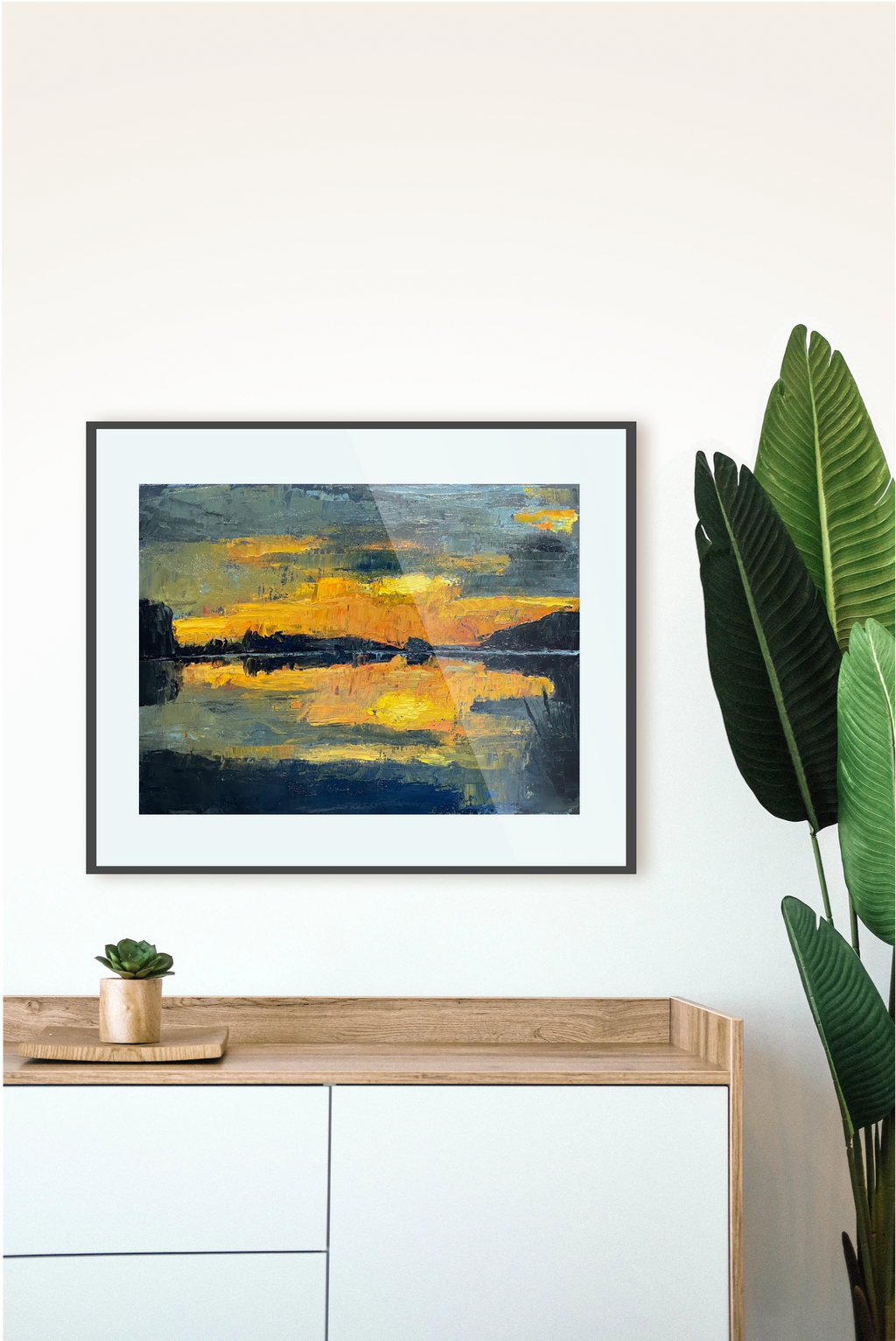 Framed abstract artwork on a wall with a console table and plant in the foreground