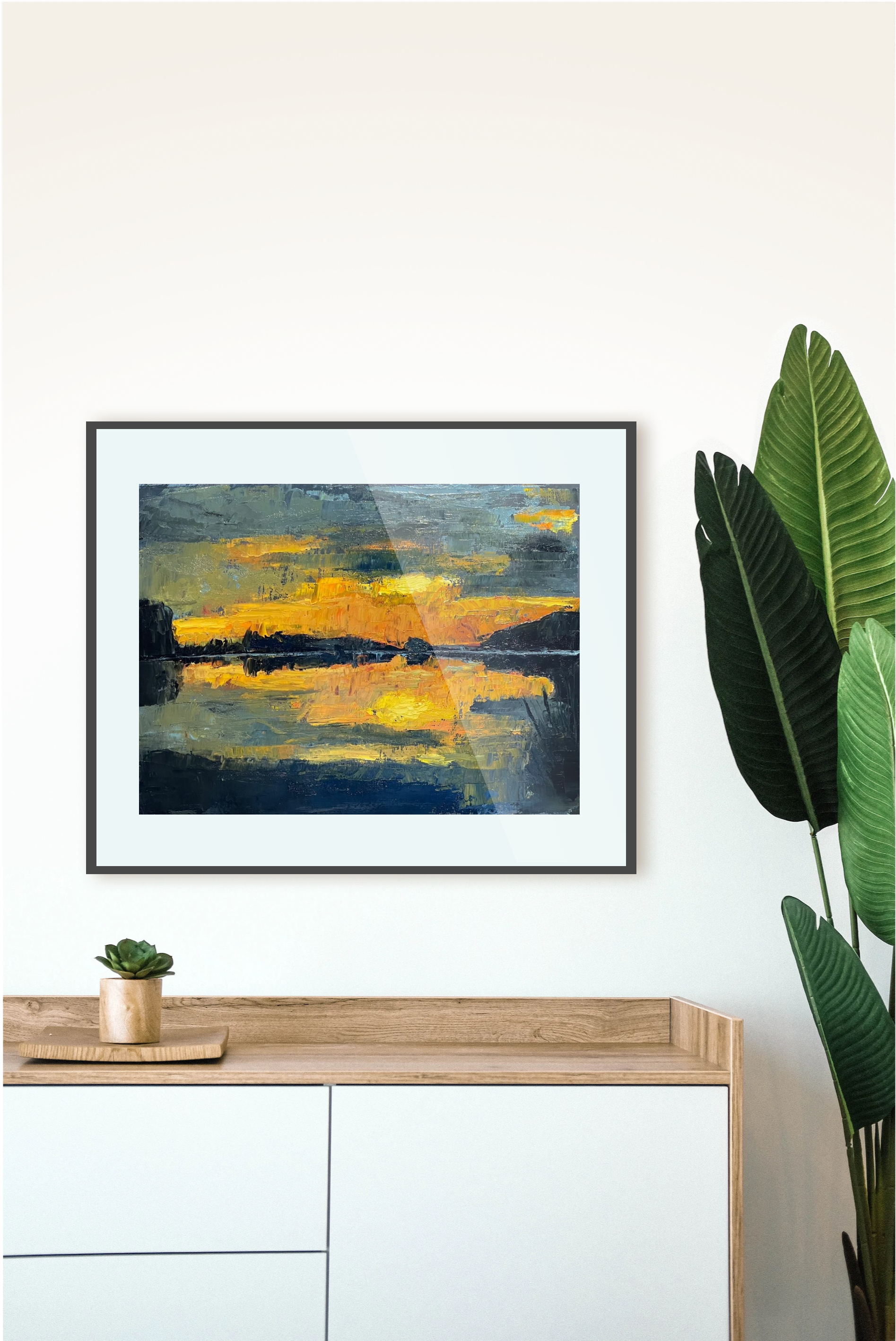 Framed abstract artwork on a wall with a console table and plant in the foreground