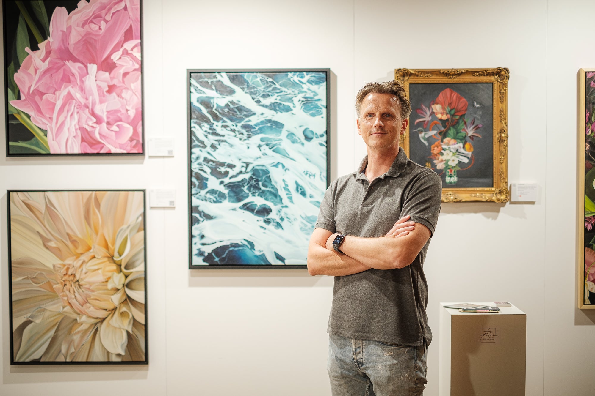 Roman van Gelder standing in front of a wall with framed artworks including floral and abstract pieces.