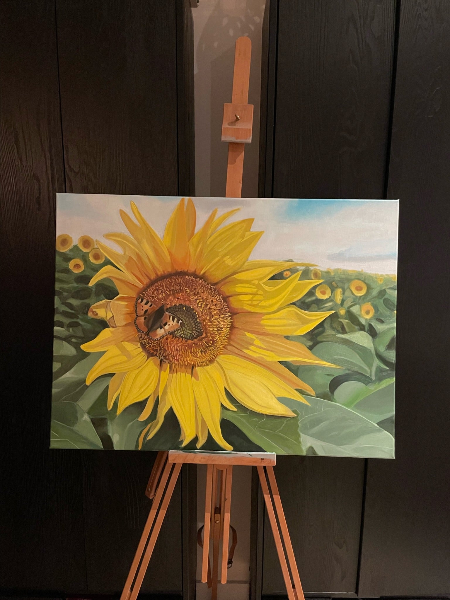 Painting of a sunflower on an easel against a dark background