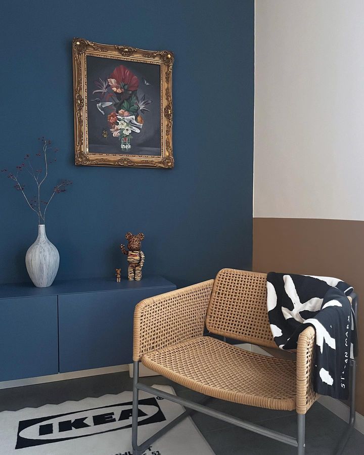 Wicker chair with a black and white blanket against a blue wall with a framed picture.