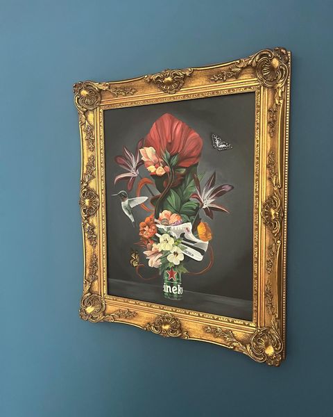 Decorative painting with flowers and a butterfly in an ornate gold frame on a blue wall.