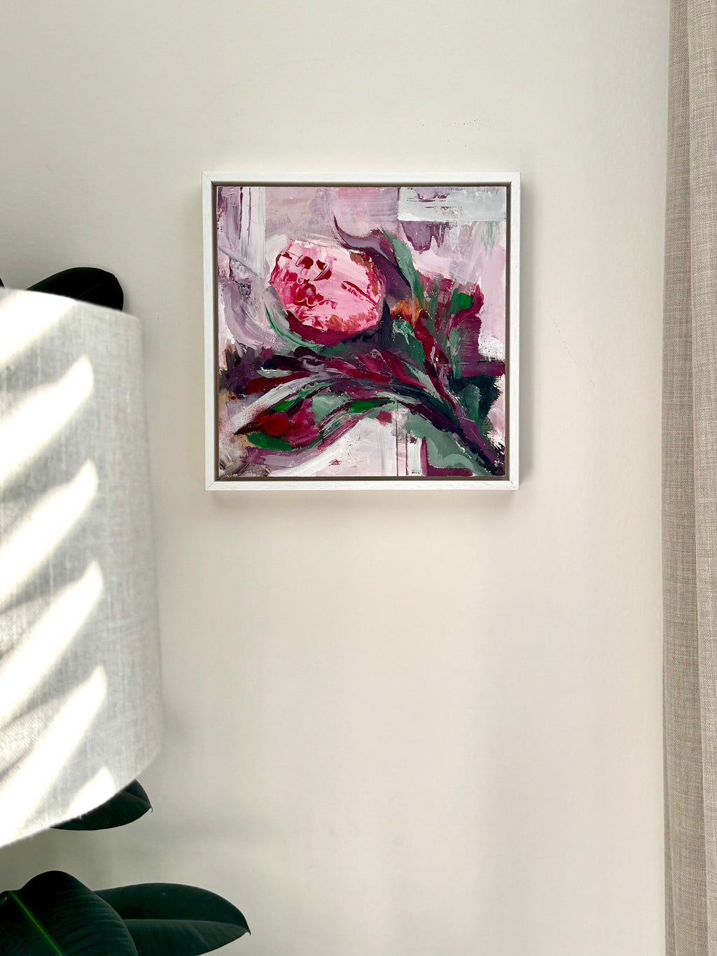 Framed abstract art piece on a wall with a lamp and plant in the background
