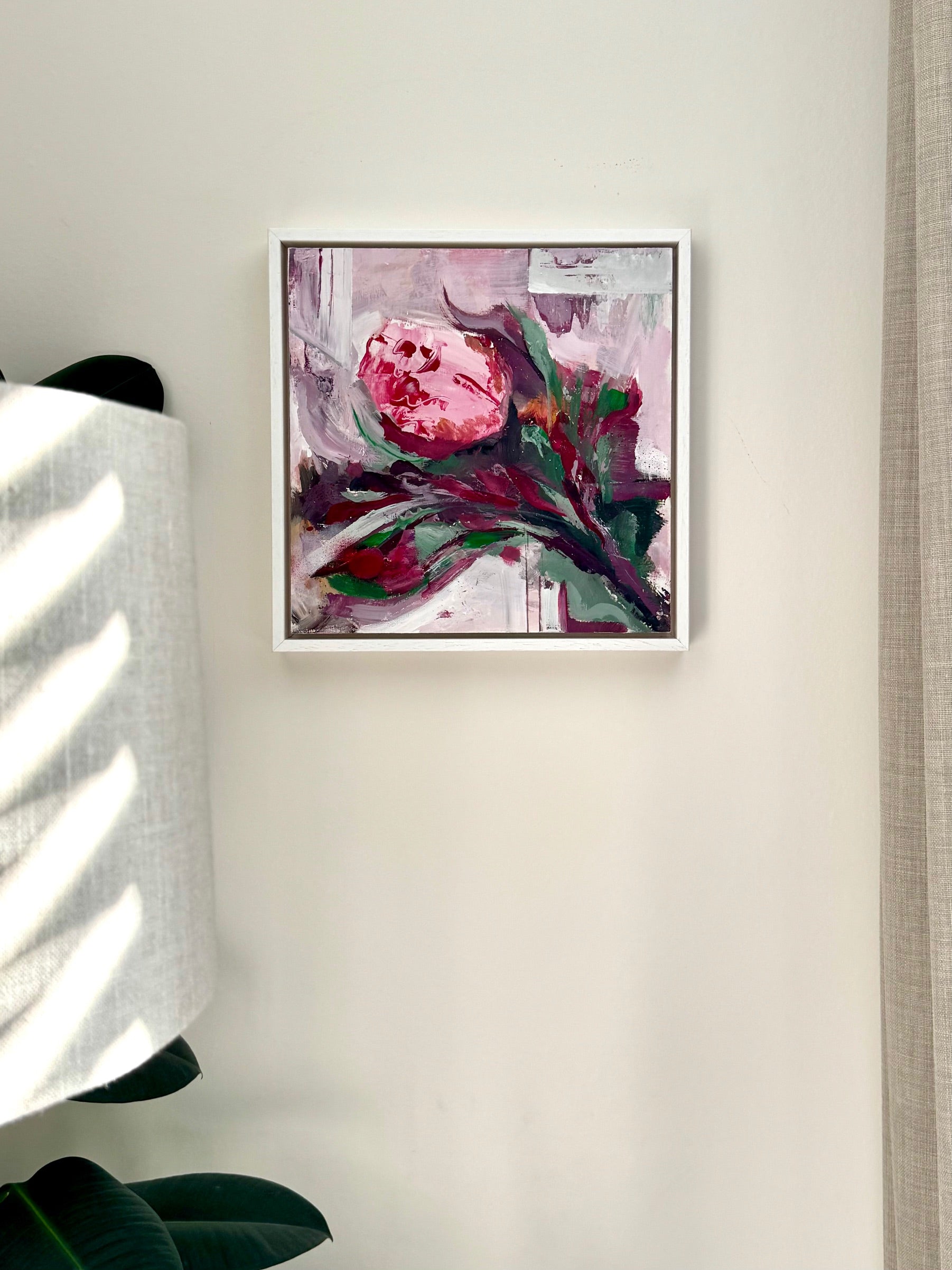 Framed abstract art piece on a wall with a lamp and plant in the background